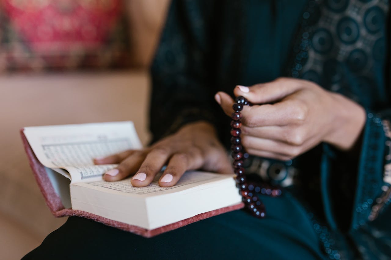 Close-up of hands holding prayer beads and an open book, symbolizing faith and tradition.